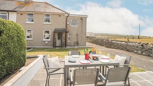 A dining area with a table set for four, a stone wall, and a house in the background. - Morlais (Ty Croes)