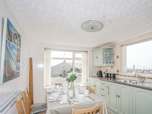 A kitchen with a dining table set for four, a view of the outside, and a cabinet with decorative items. - Morlais (Ty Croes)