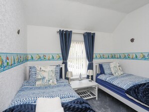 A room with two beds, a small table, a lamp, and a window with curtains. - Morlais (Ty Croes)