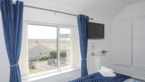 A bedroom with a bed, a dresser, a television, and a window with curtains. - Morlais (Ty Croes)