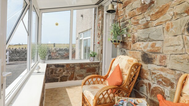 A cozy room with a wicker chair, a window with a view of the countryside, and a stone wall. - Morlais (Ty Croes)