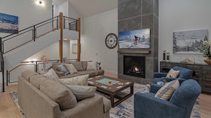 A modern living room with a fireplace, a staircase, and a large clock on the wall.