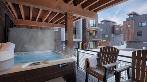 Un jacuzzi en un balcón con sillas de madera, con vistas a un complejo de edificios moderno.