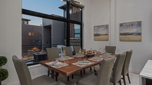 A dining area with a wooden table set for six, large windows, and two landscape paintings on the wall. - Ski Shuttle + Hot Tub + New Home - Uptown House (Steamboat Springs)