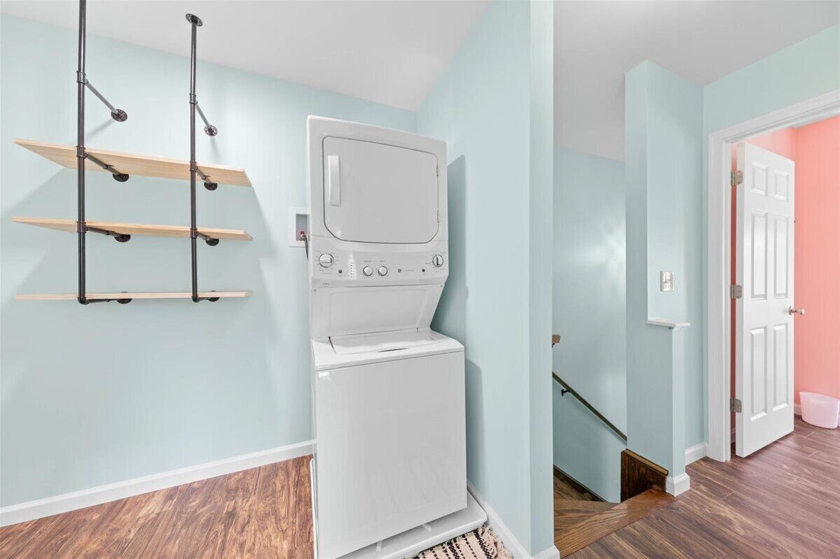 A laundry room with a white washer and dryer, wooden shelves, and a staircase leading to another room.