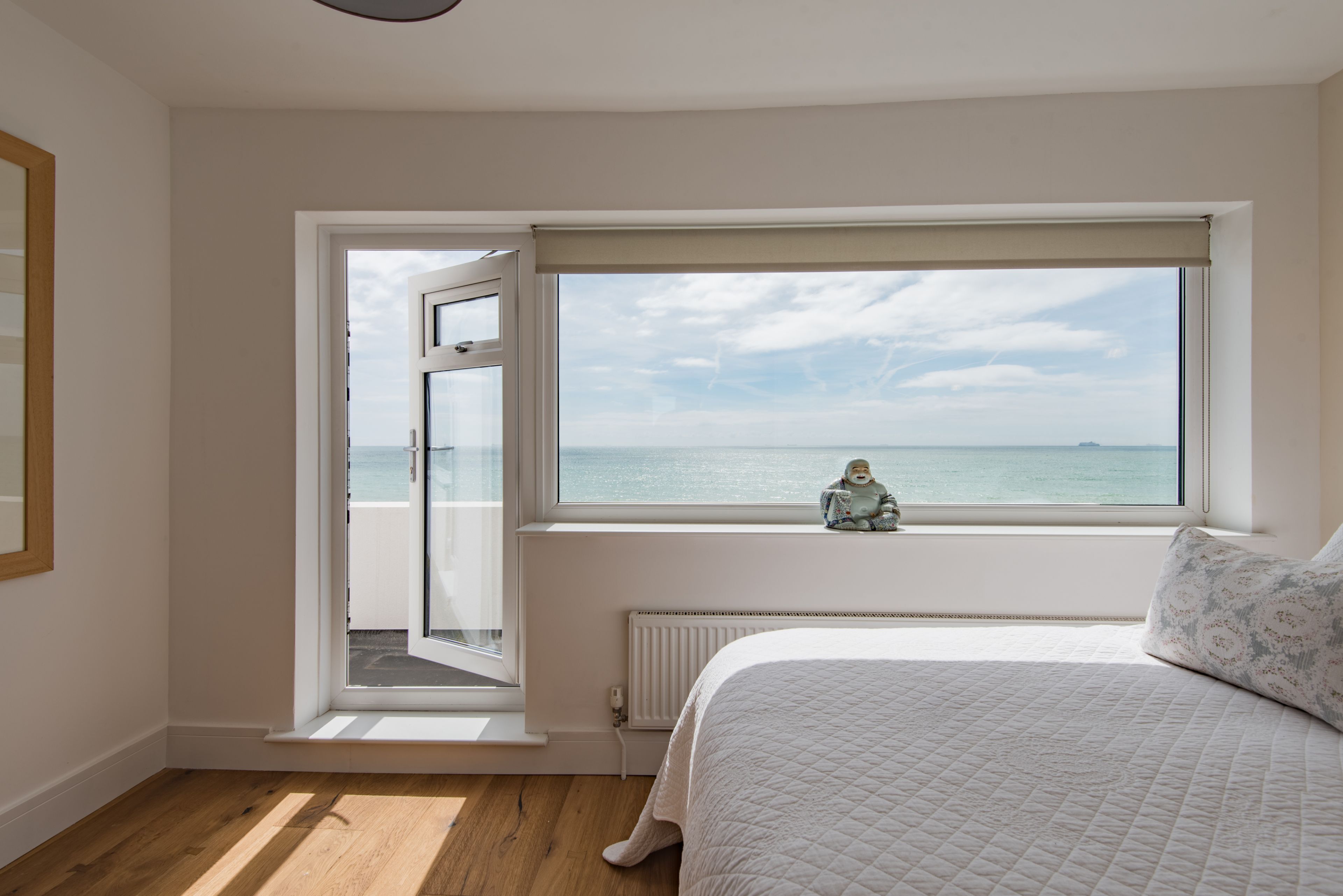A bedroom with a large window overlooking the sea, a bed with a quilted cover, and a radiator below the window.