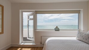 Quarto com uma grande janela vista para o mar, cama com colcha acolchoada e radiador abaixo da janela.