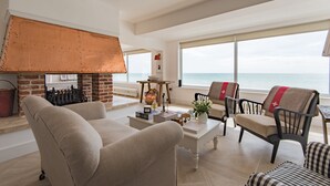 Uma sala de estar com lareira, assentos e vista para o mar.