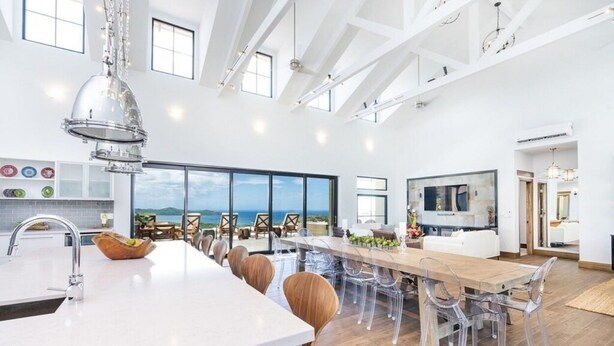 Una cocina espaciosa con una isla grande, sillas traslúcidas y vista al mar.