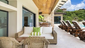 Un área de descanso moderna al aire libre con techo de madera, mobiliario de mimbre y zona de estar junto a la piscina.