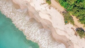 Vista aérea de una playa con aguas turquesas cristalinas, una orilla arenosa y algo de vegetación.