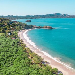 Uma área costeira com uma praia de areia, águas turquesa cristalinas e vegetação exuberante.