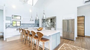 Una cocina moderna con una isla central, taburetes de madera, electrodomésticos de acero inoxidable y un salpicadero de mármol.