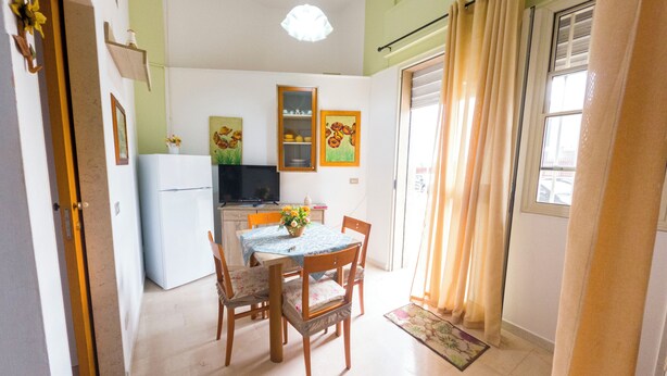 Une cuisine de taille réduite comprenant un réfrigérateur, une table à manger avec des chaises et un téléviseur posé sur un meuble.