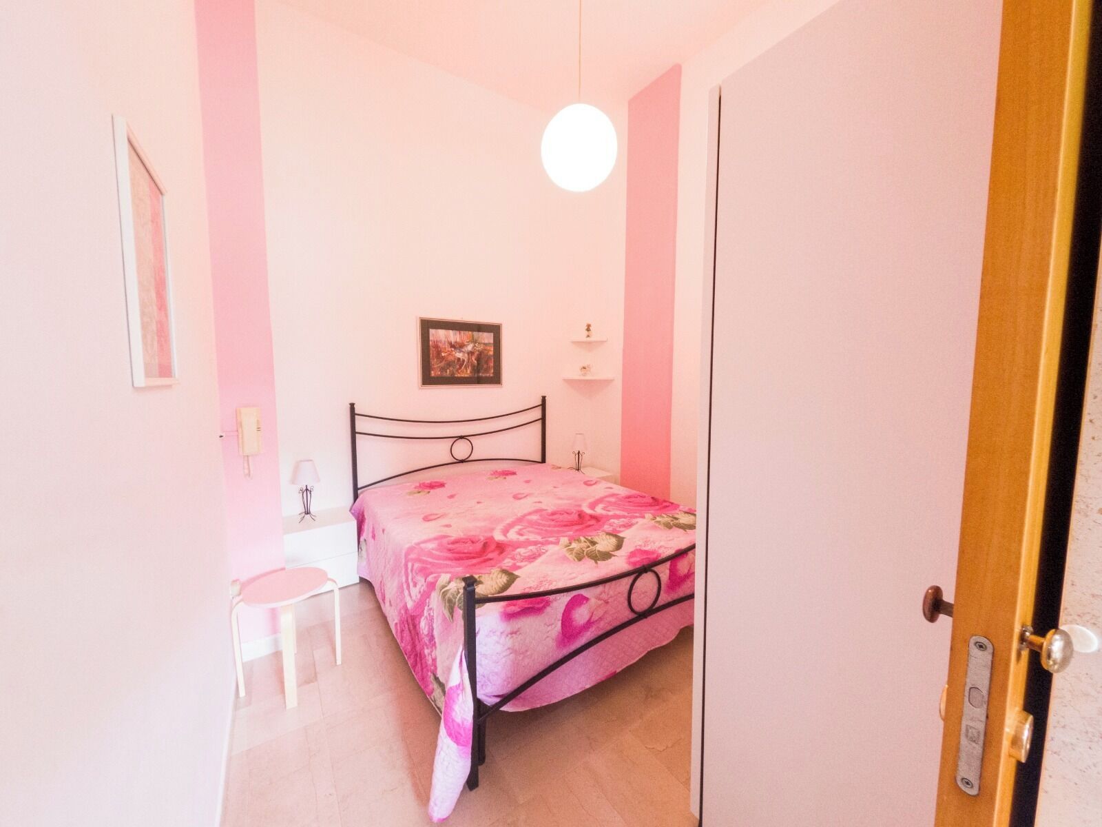 A bedroom with a bed, a chair, a bedside table, a lamp, and a picture on the wall.