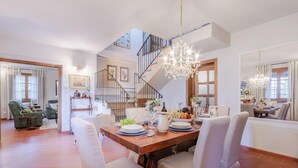Ein geräumiger Essbereich mit hoher Decke, einer Treppe und einem Chandelier.