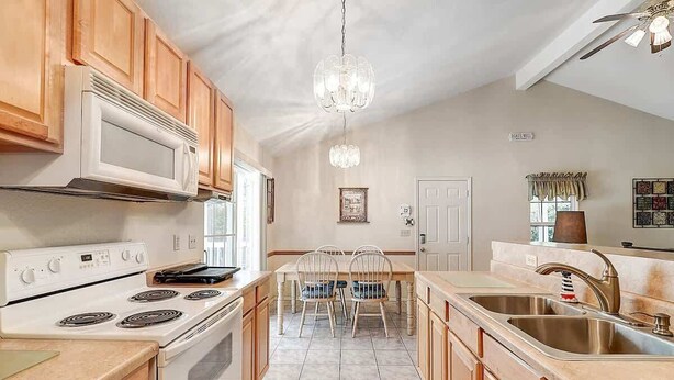 A kitchen with wooden cabinets, a white stove, a chandelier, and a dining area with chairs. - Seashell Memories (Rockport)