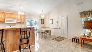 A kitchen with wooden cabinets, a microwave, a dining area with a table and chairs, and a chandelier. - Seashell Memories (Rockport)