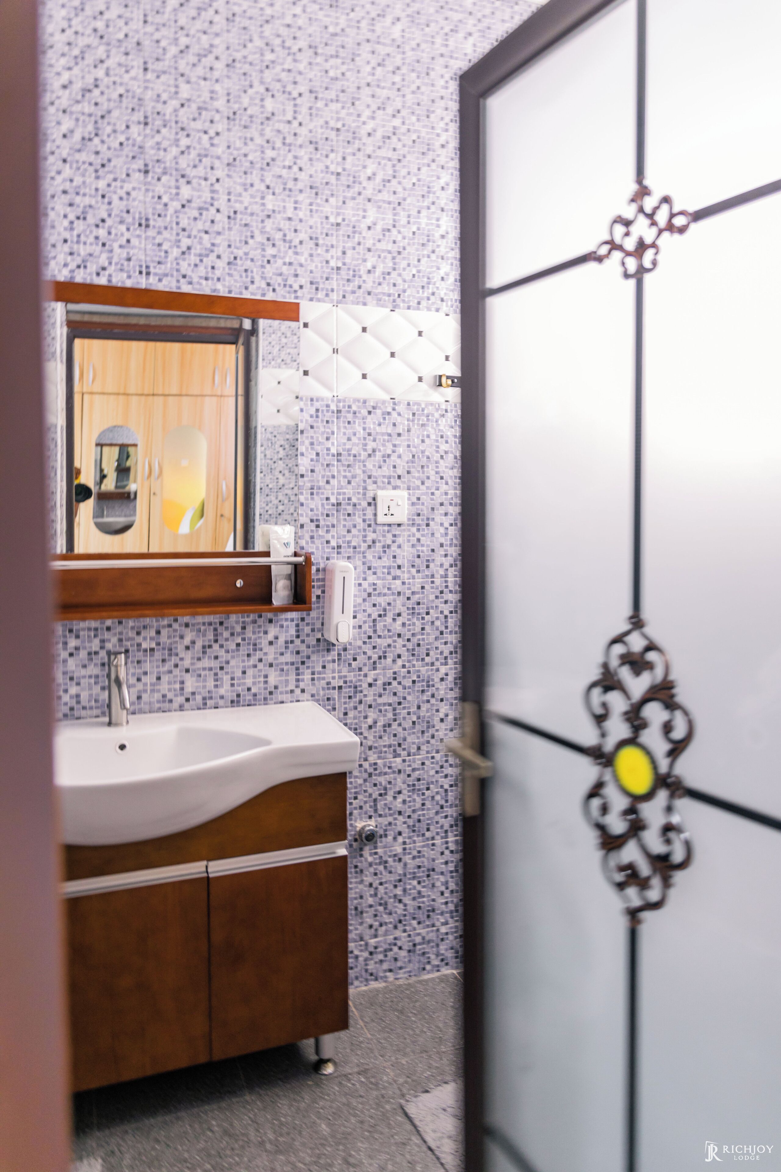 A bathroom with a wooden vanity, a white sink, a mirror, and a tiled wall.