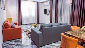 Una sala de estar moderna con un sofá gris, sillones naranja, una mesa de centro de madera y un televisor montado en la pared.