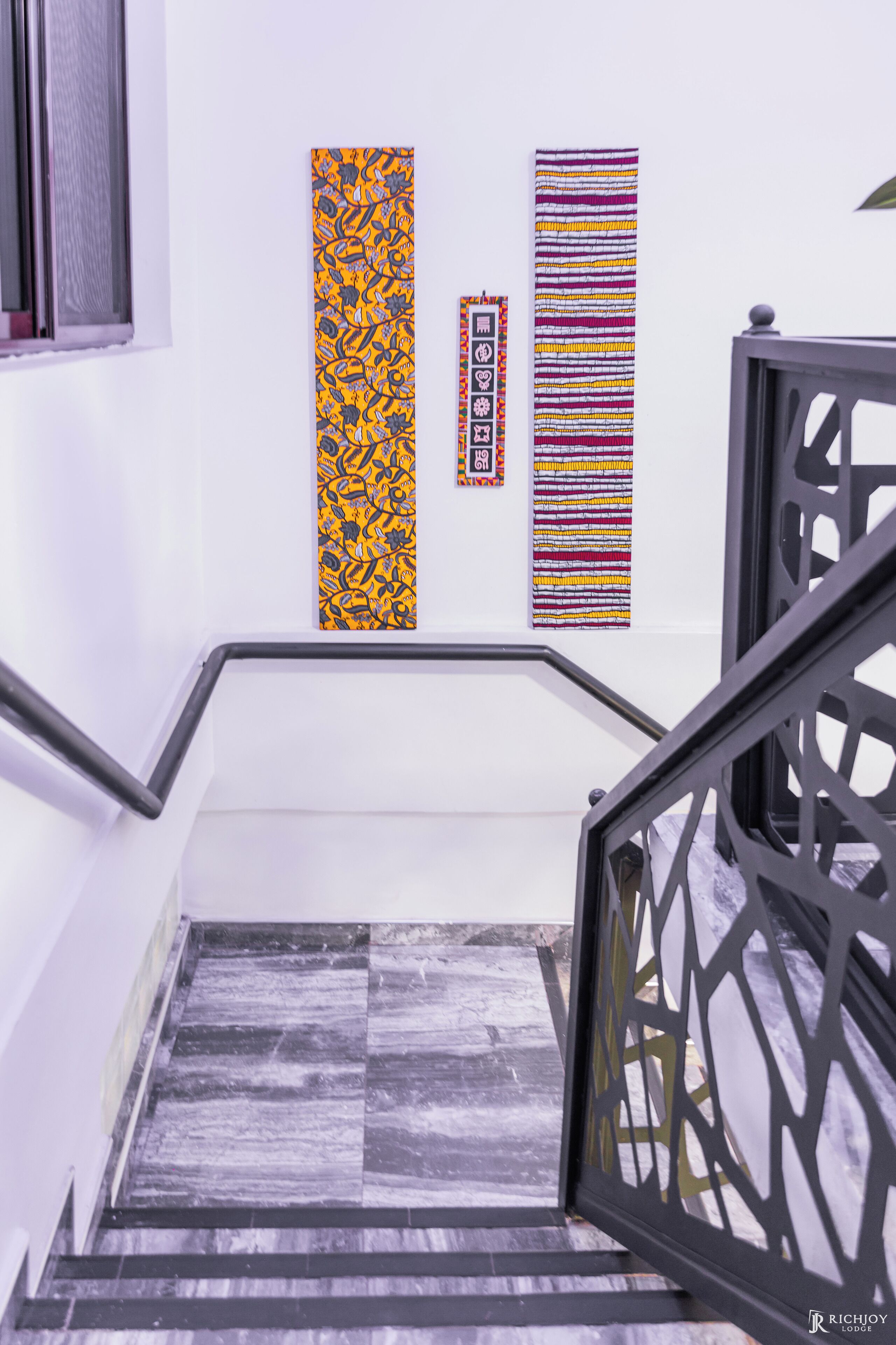 A staircase with a black metal railing, white walls, and three vertical artworks on the wall.
