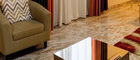 Un salon avec un canapé beige, un coussin décoratif à motifs, une table basse en bois et une grande fenêtre ornée de rideaux orange.
