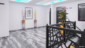 Un interior moderno con piso de mármol, una escalera con barandilla decorativa y dos plantas en macetas.