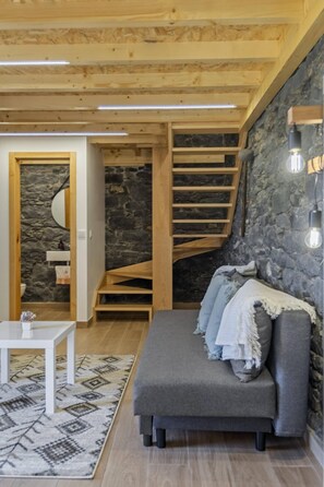 A cozy room with a wooden staircase, a grey sofa, and a white table. - Mountain Retreat by Homie (Porto Moniz)