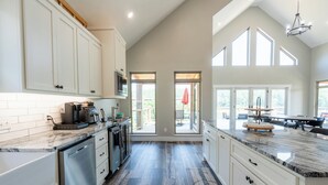 A spacious kitchen with white cabinets, a granite countertop, and a view to the outside.