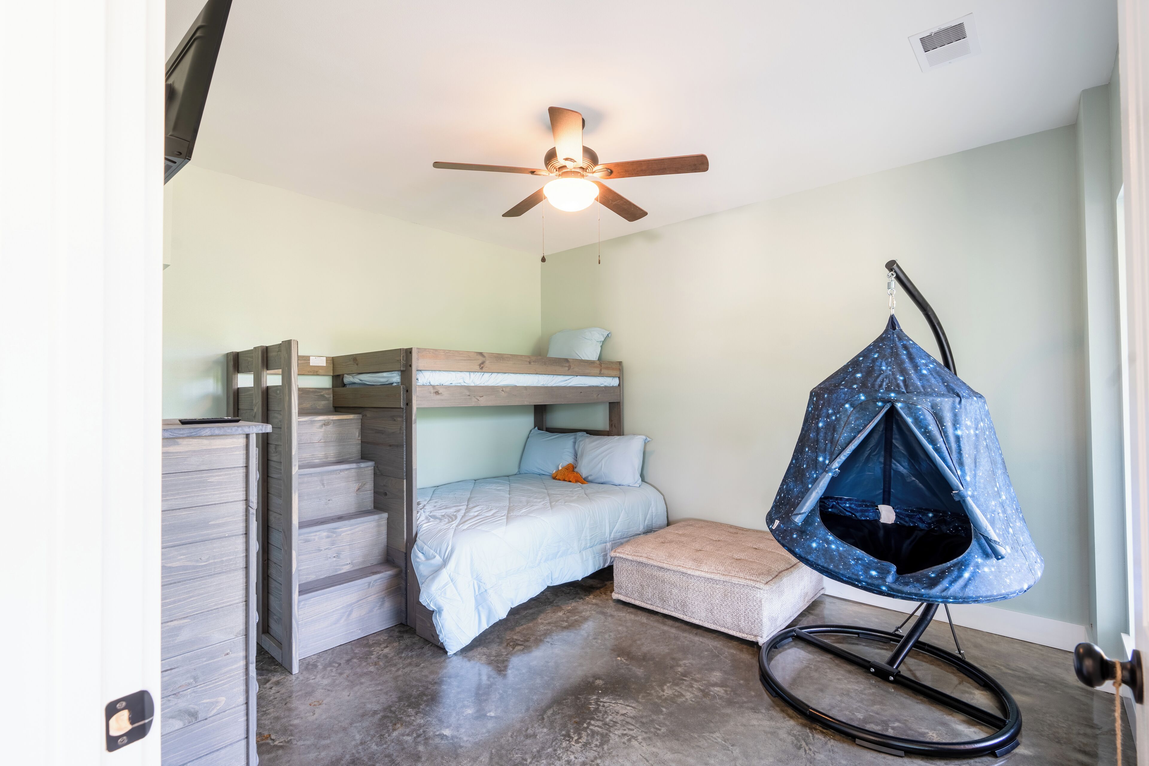 A compact room with a bunk bed, a ceiling fan, and a hanging chair.