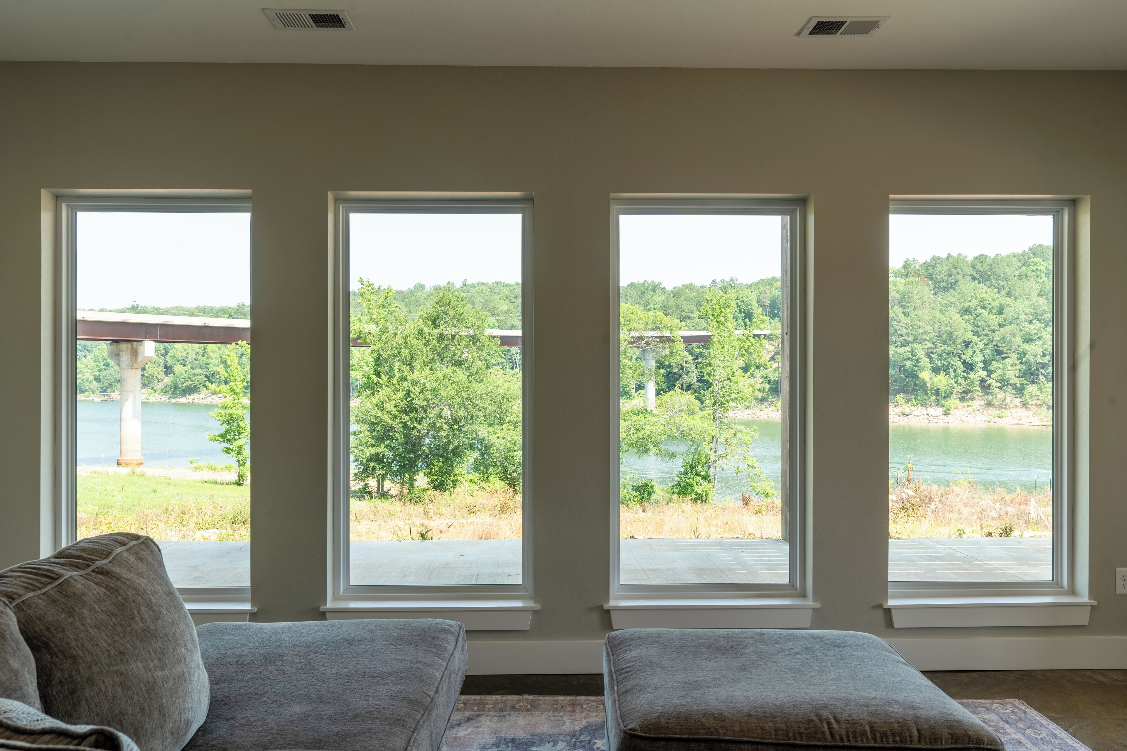 A room with a large window overlooking a lake and trees, a gray sofa, and a patterned rug.