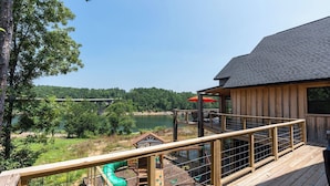 A wooden deck with a playground, a small house, and a view of a lake and forest.