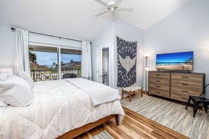 Een slaapkamer met een groot bed, een plafondventilator, een wandtapijt, een dressoir en uitzicht op het strand.