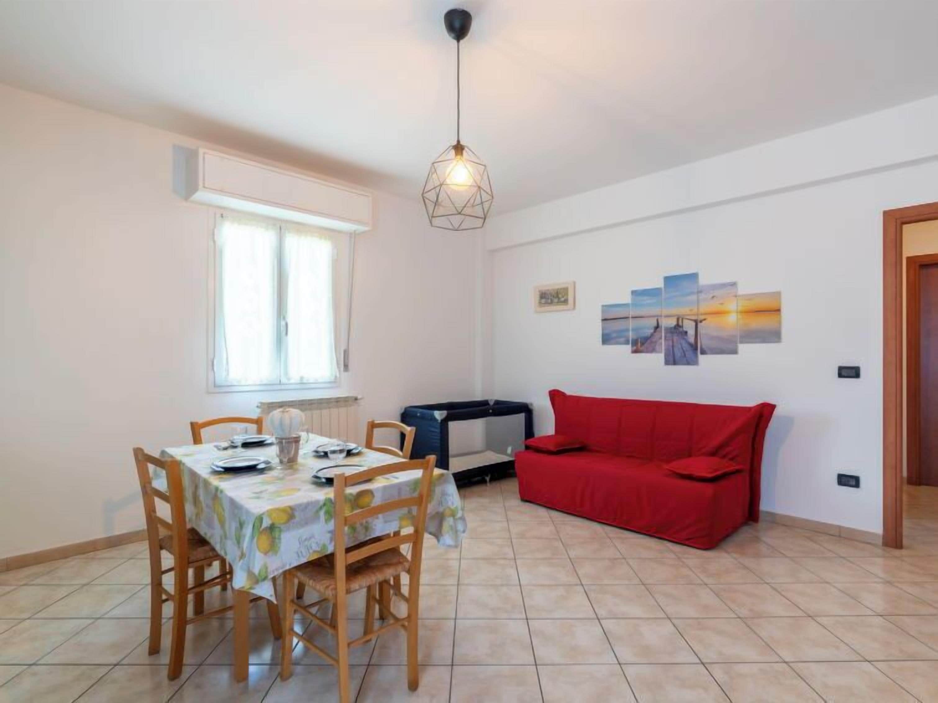 A dining area with a table set for four, a red sofa, and a wall with three paintings.