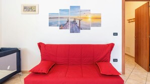 A room with a red bed, a wall-mounted artwork of a sunset over water, and a door to the right. - Apartment Ulivo by Interhome (Chiusanico)