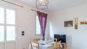 A dining area with a table set for two, a television on a stand, and a window with curtains. - Apartment Mimosa by Interhome (Chiusanico)