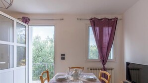 A dining area with a table set for four, a television on a stand, and a window with purple curtains. - Apartment Mimosa by Interhome (Chiusanico)