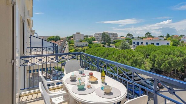 A balcony with a table set for dining, overlooking a residential area with trees and buildings. - Parc de Pontaillac by Interhome (Vaux Sur Mer)