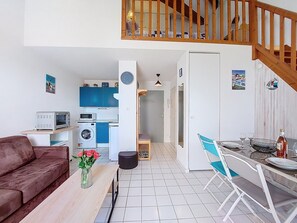 A compact living space with a kitchenette, a dining area, a sofa, and a staircase.