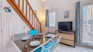 A dining area with a wooden staircase, a TV, and a window with curtains. - Parc de Pontaillac by Interhome (Vaux Sur Mer)