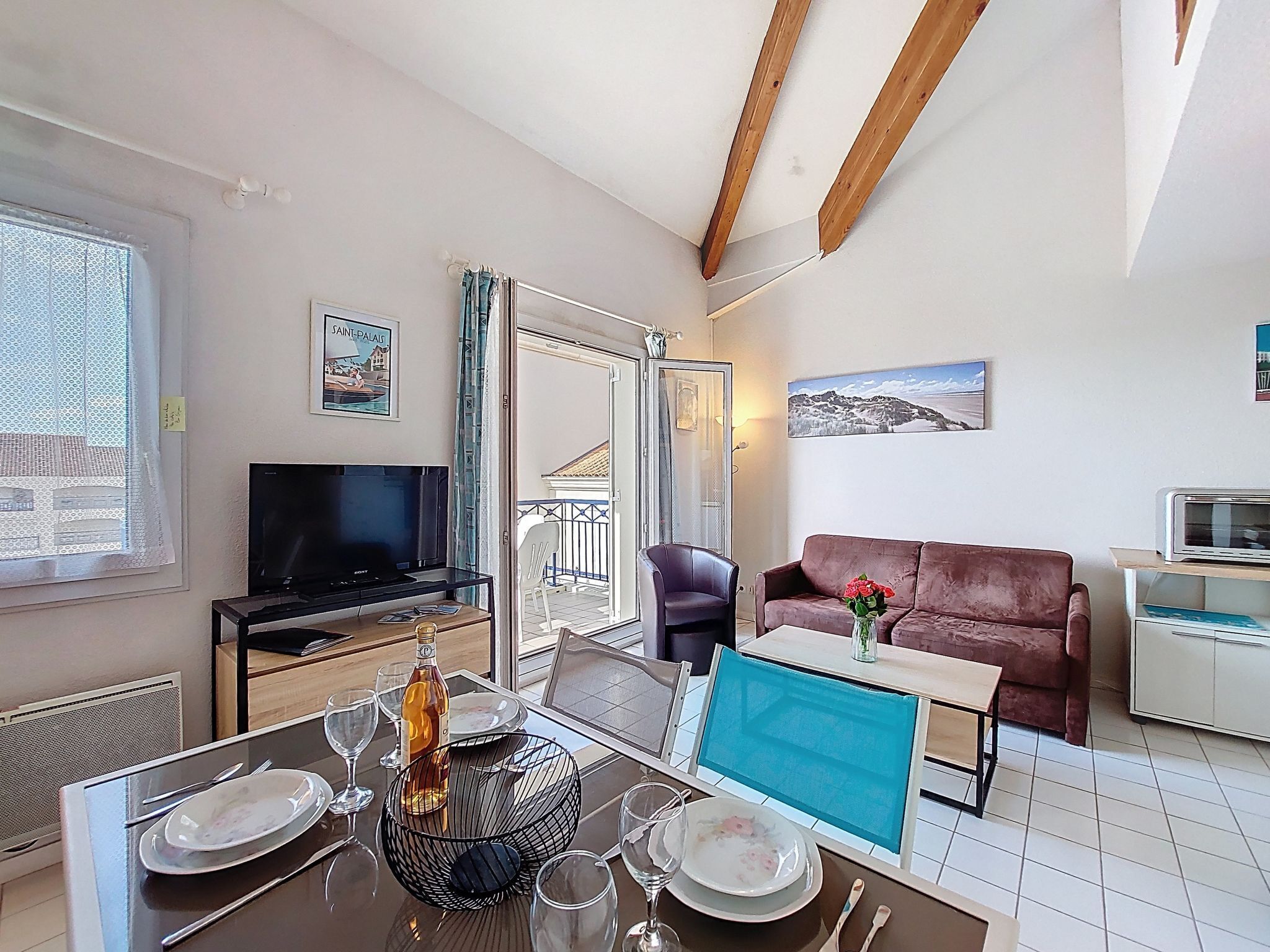 A modern living room with a dining area, a television, a sofa, and a balcony.
