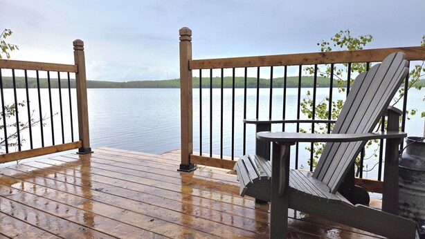 Een houten terras met uitzicht op een meer, een Adirondack stoel en een kleine tafel.