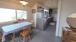Een kleine keuken met een koelkast, houten kastjes en een eethoek met een tafel en stoelen.