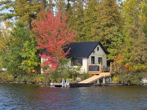 A cabin with a dock extending into a lake, surrounded by autumn foliage.