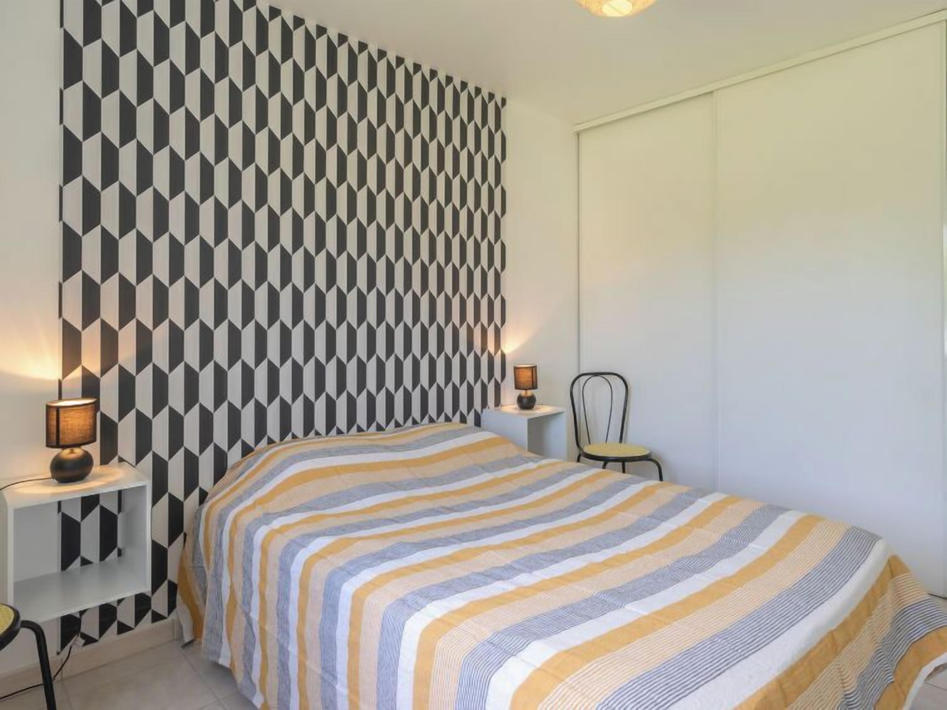 Ein Schlafzimmer mit Wand im geometrischen Muster, einer gestreiften Bettdecke, zwei Nachttischlampen und einem Sessel.