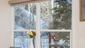 A room with a wooden table and chairs, a white vase with flowers, and a large window with a view of trees and a snowy landscape. - Mountainside Inn 109 1 Bedroom Hotel Room by Alpine Lodging Telluride (Telluride)