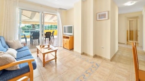 Uma sala de estar moderna com sofá, mesa de centro e televisão. Há uma varanda com mobiliário de exterior.