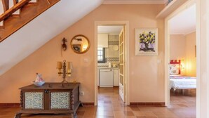 Un hall d’entrée spacieux avec un escalier en bois, une commode décorative, un miroir et un tableau.