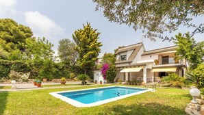 Une maison avec une piscine, entourée d’une pelouse bien entretenue et de diverses plantes.