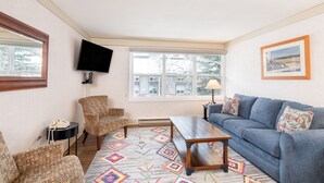 A living room with a blue sofa, patterned armchairs, a wooden coffee table, and a television mounted on the wall. - Mountainside Inn 122 1 Bedroom Condo by Alpine Lodging Telluride (Telluride)